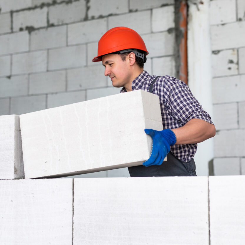 Man wearing a red helmet working, building a wall from bricks.