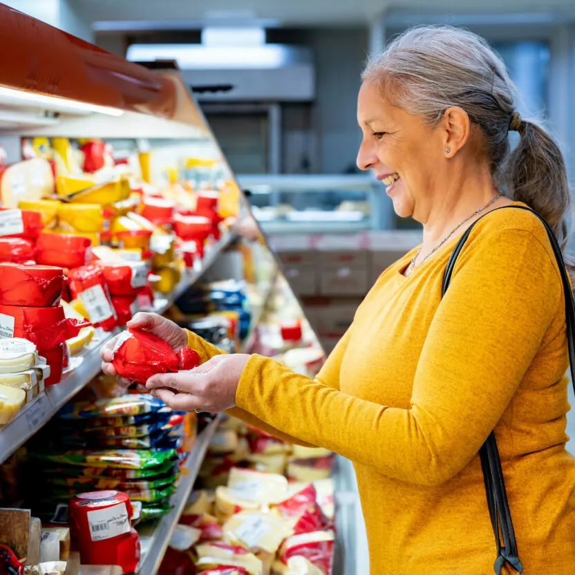 Elderly woman buying cheese in supermarket.