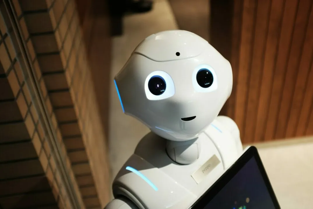 Ein weißer Roboter schaut den Betrachter an. Er hält ein Tablet in seiner Hand.