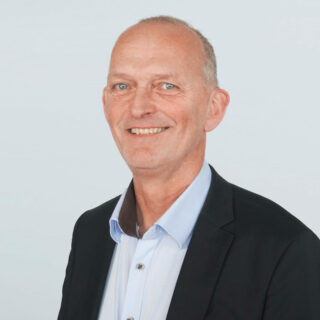 Portrait eines Mannes mit blauen Augen, hellblauem Hemd, dunklem Blazer auf einem hellen Hintergrund