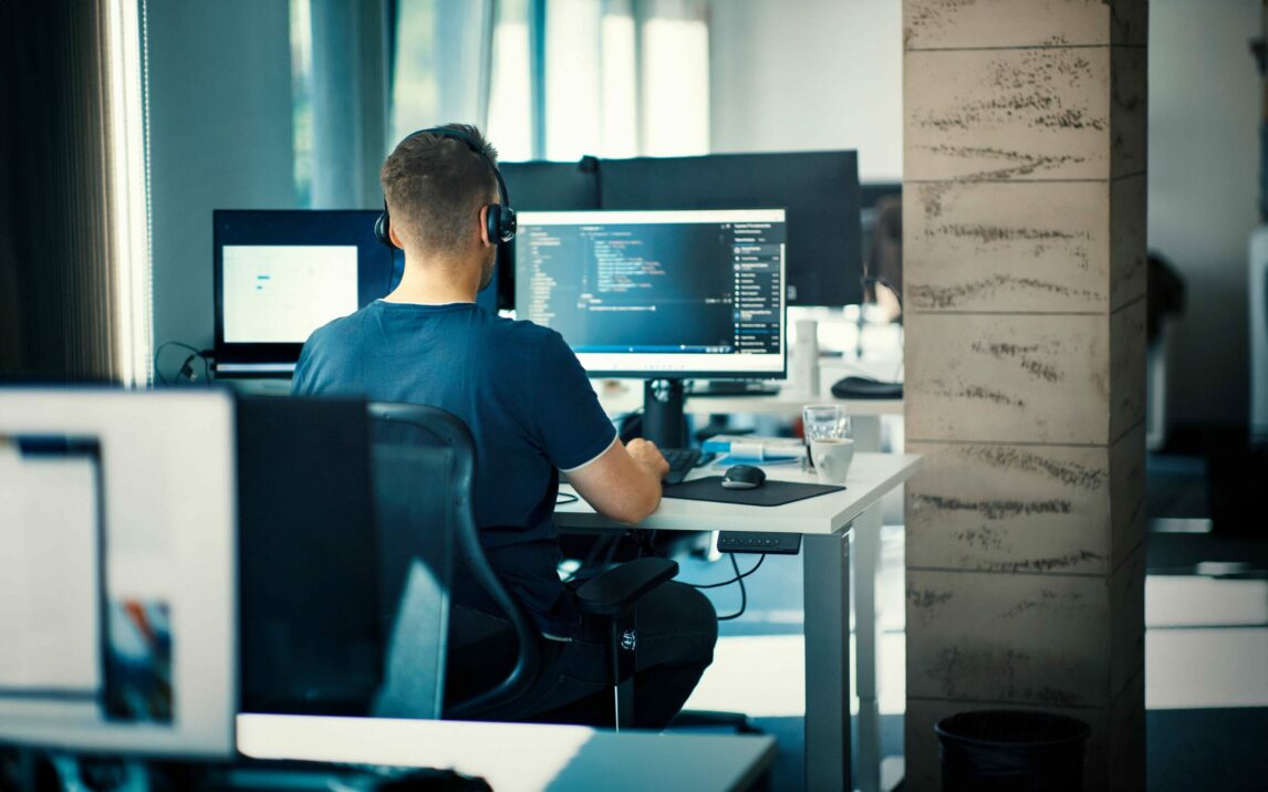 Software developer at the office.. Closeup rear view of a young man coding on multiple computers.