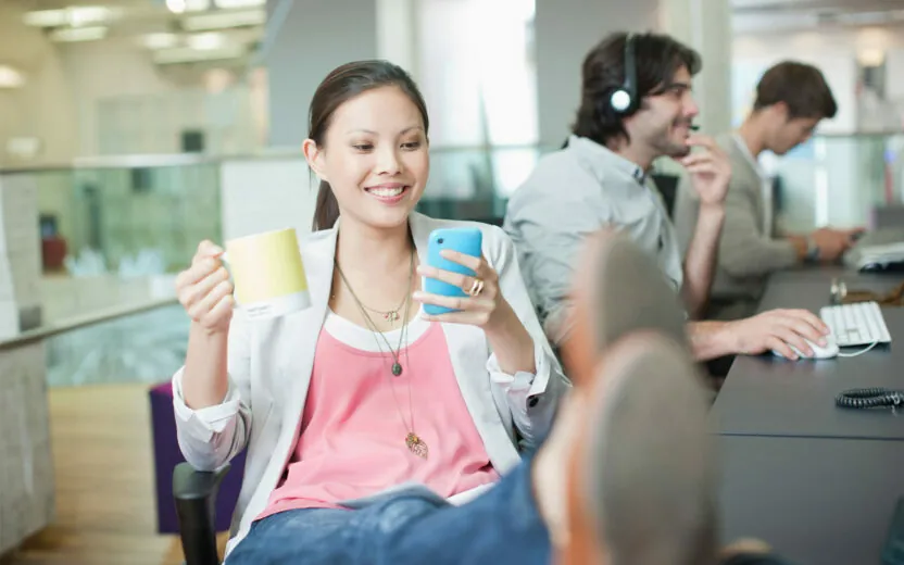 Businesswoman drinking coffee and text messaging with feet up in office