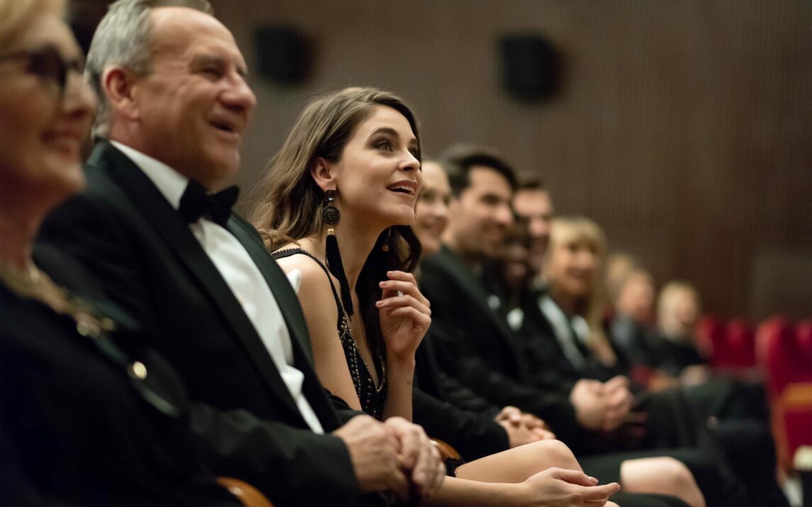 Side view of multi ethnic audience sitting in the opera. Men and women are watching theatrical performance. They are in elegant wear.