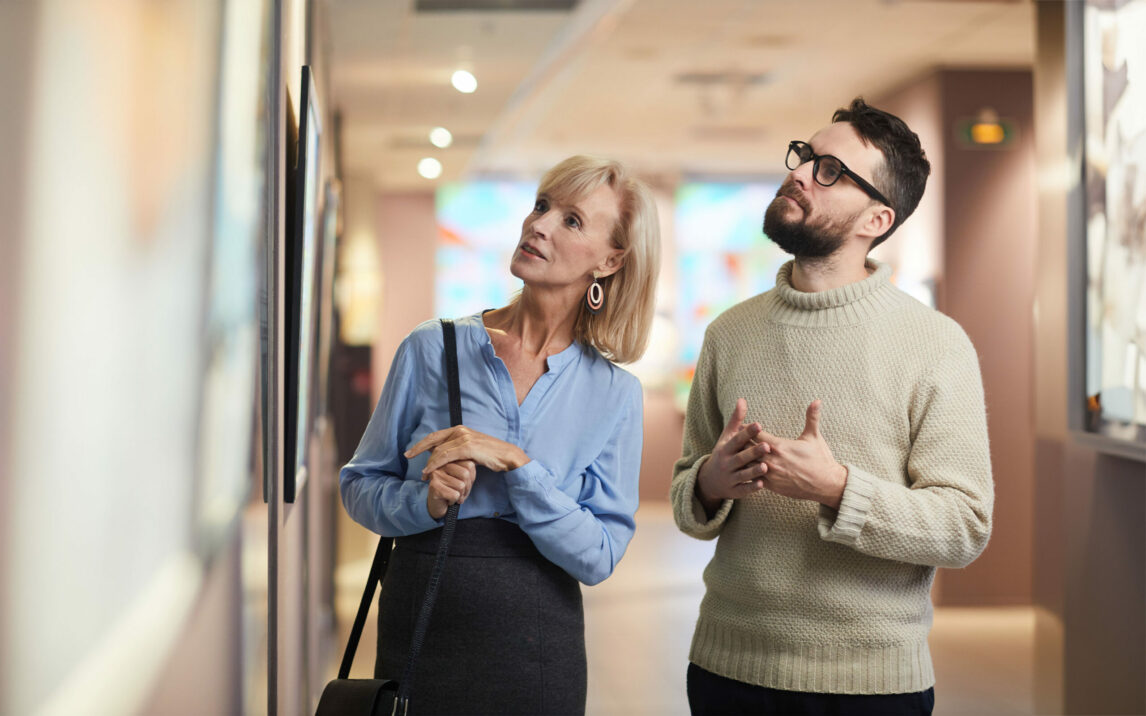 Waist up portrait of modern mature couple looking at paintings while enjoying exhibition in art gallery or museum