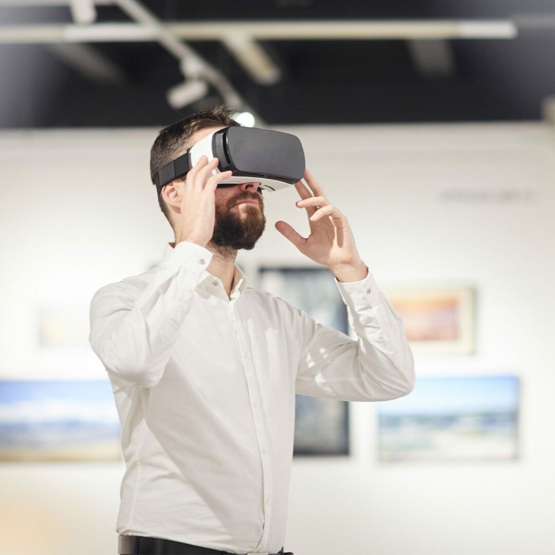 Side view portrait of modern bearded man wearing VR gear while enjoying immersive experience during exhibition in art gallery, copy space
