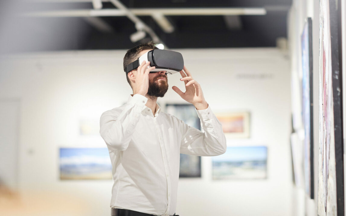 Side view portrait of modern bearded man wearing VR gear while enjoying immersive experience during exhibition in art gallery, copy space