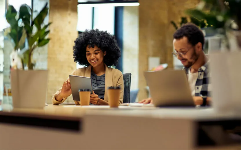 Two young business people sitting at the desk, using modern technologies while working together in coworking space. Office life, teamwork and business