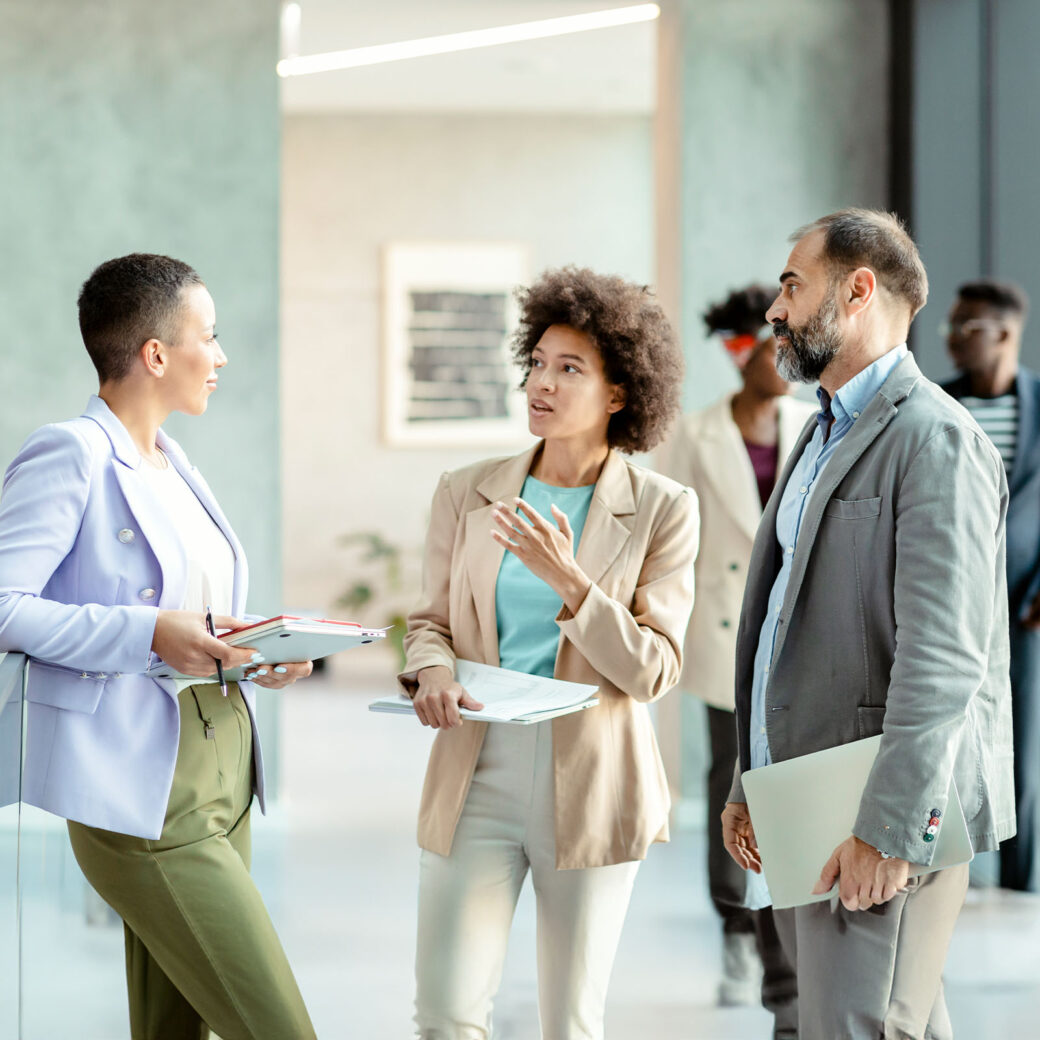 Diverse group of businesspeople discussing work while standing together in a bright modern office corridor
