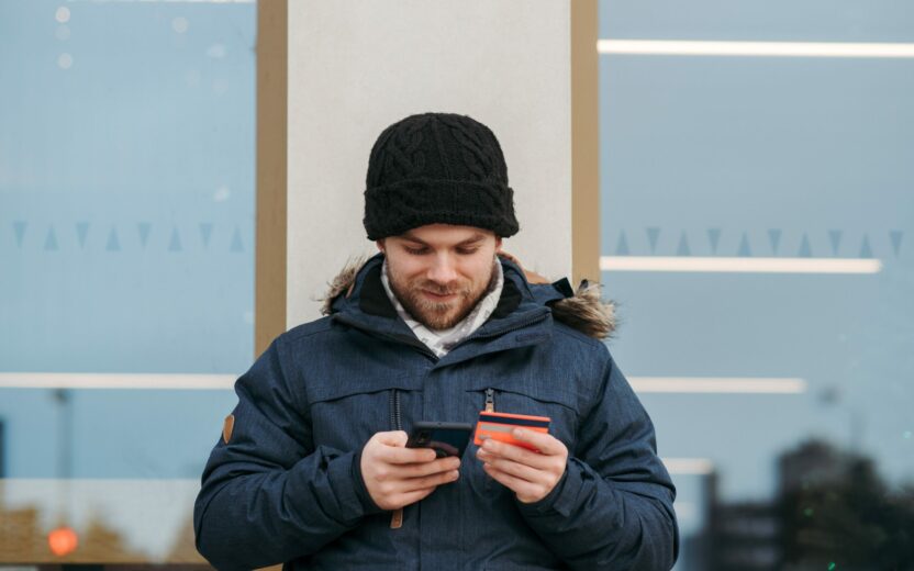 Lächelnder Mann mit Handy und Kreditkarte in der Hand arbeitet an seinem B2B-Marktplatz