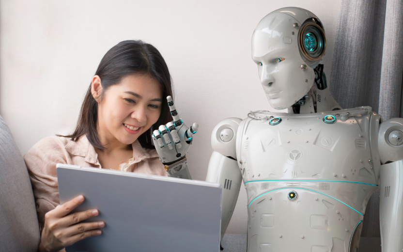 valantic BARC 2024 - Eine Frau sitzt neben einem Roboter und sie schauen gemeinsam in einen Laptop.