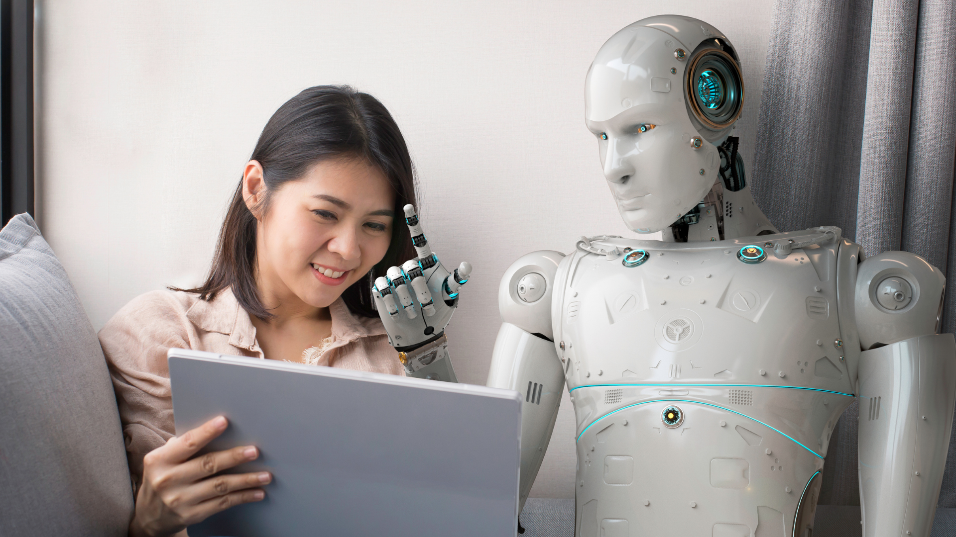 A woman smiles at a laptop screen while sitting next to a humanoid robot, which touches its chin thoughtfully.