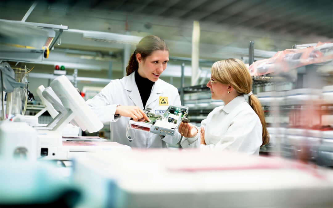 Two lab technicians in white coats discuss a Biotronik device in a laboratory setting. Biotronik valantic Supply Chain Excellence Day APS Software wayRTS