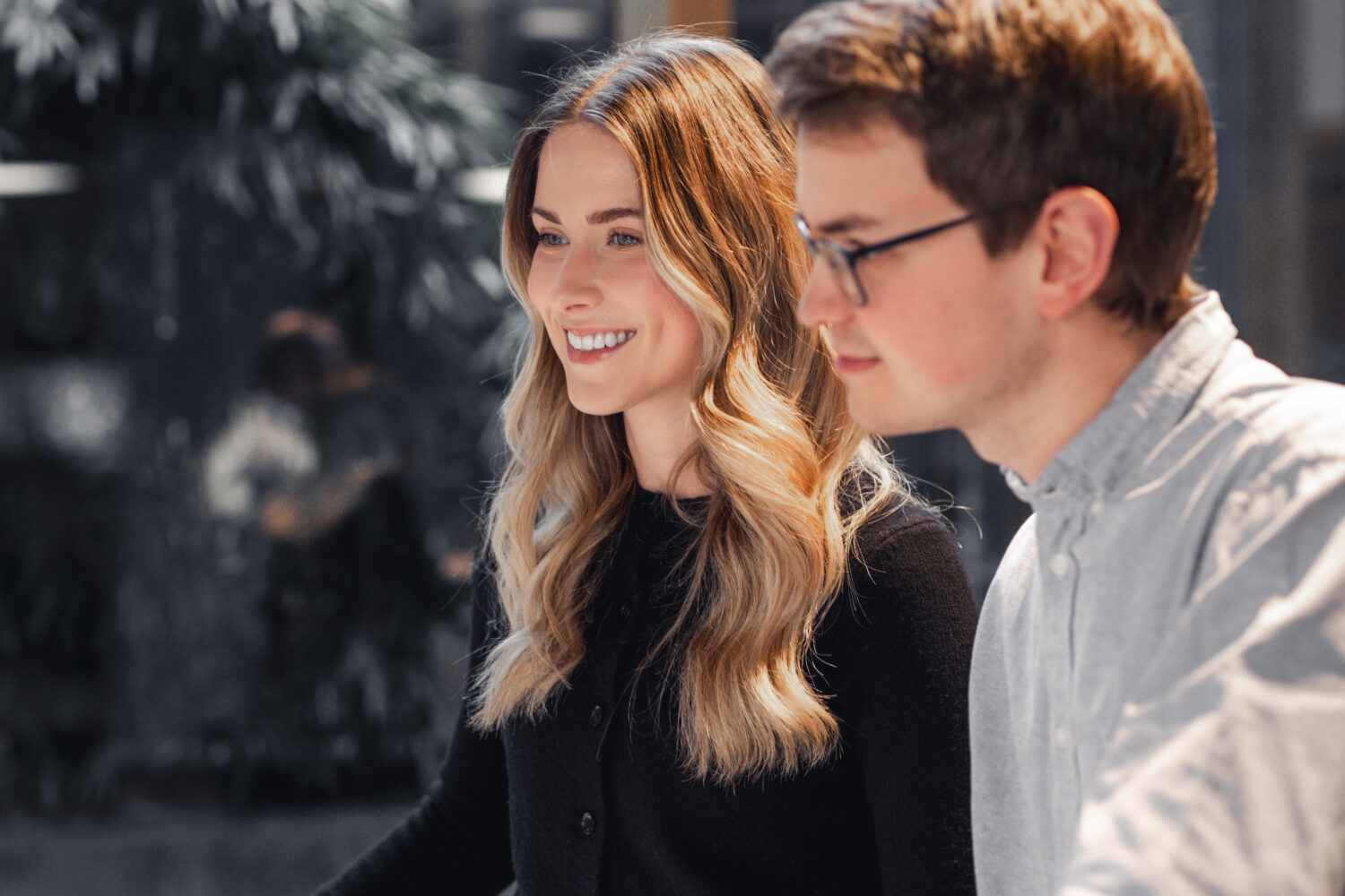 Eine lächelnde junge Frau mit langen blonden Haaren und ein junger Mann mit Brille und weißem Hemd im Profil.