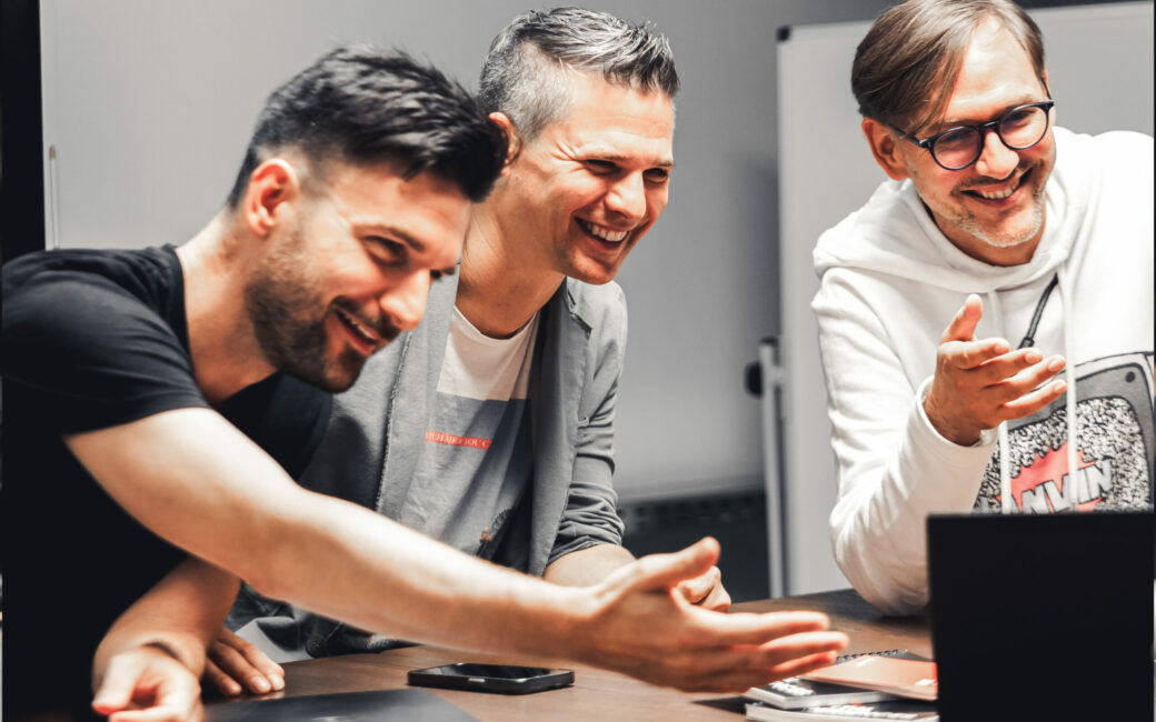 Drei valantic Austria Mitarbeiter die sich über die neuen Social Creations freuen und vor einem Laptop sitzen.