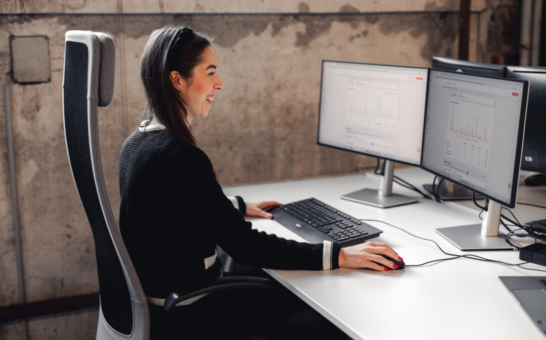 Eine junge lächelnde Frau mit dunkler Kleidung sitzt an ihre Arbeitsplatz.