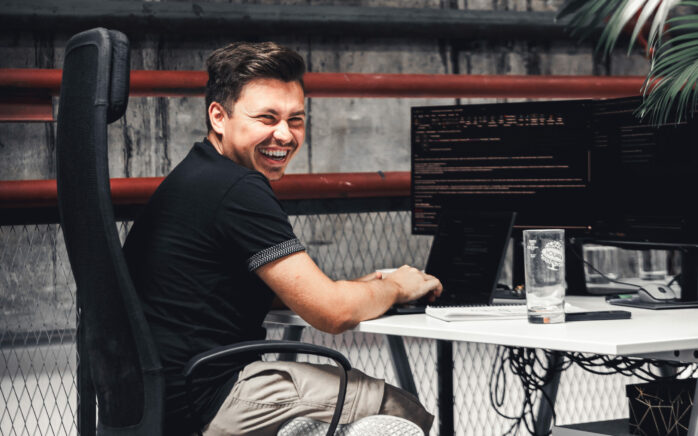 Junger Web-Entwickler sitzt vor seinem Rechner und lacht.