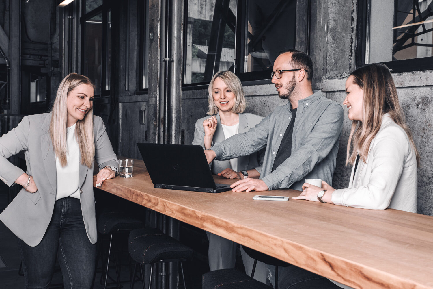 Vier Mitarbeiter*innen von valantic Austria stehen zusammen an einem Holztisch und bearbeiten eine Präsentation auf einem Laptop.