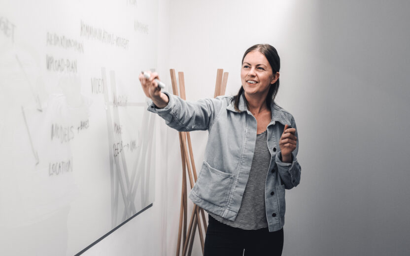 Junge Frau präsentiert Projetkidee an einem White Board.