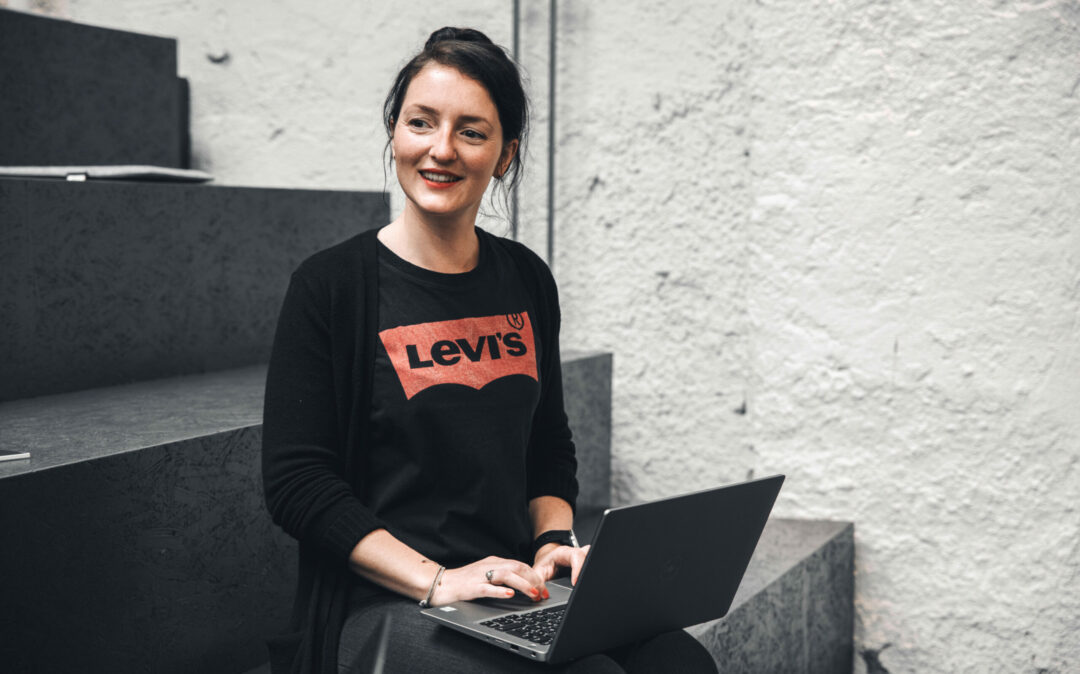 Junge Frau aus dem SEO-Team von valantic Austria sitzt auf einer Treppe und schreibt etwas auf einem Laptop.