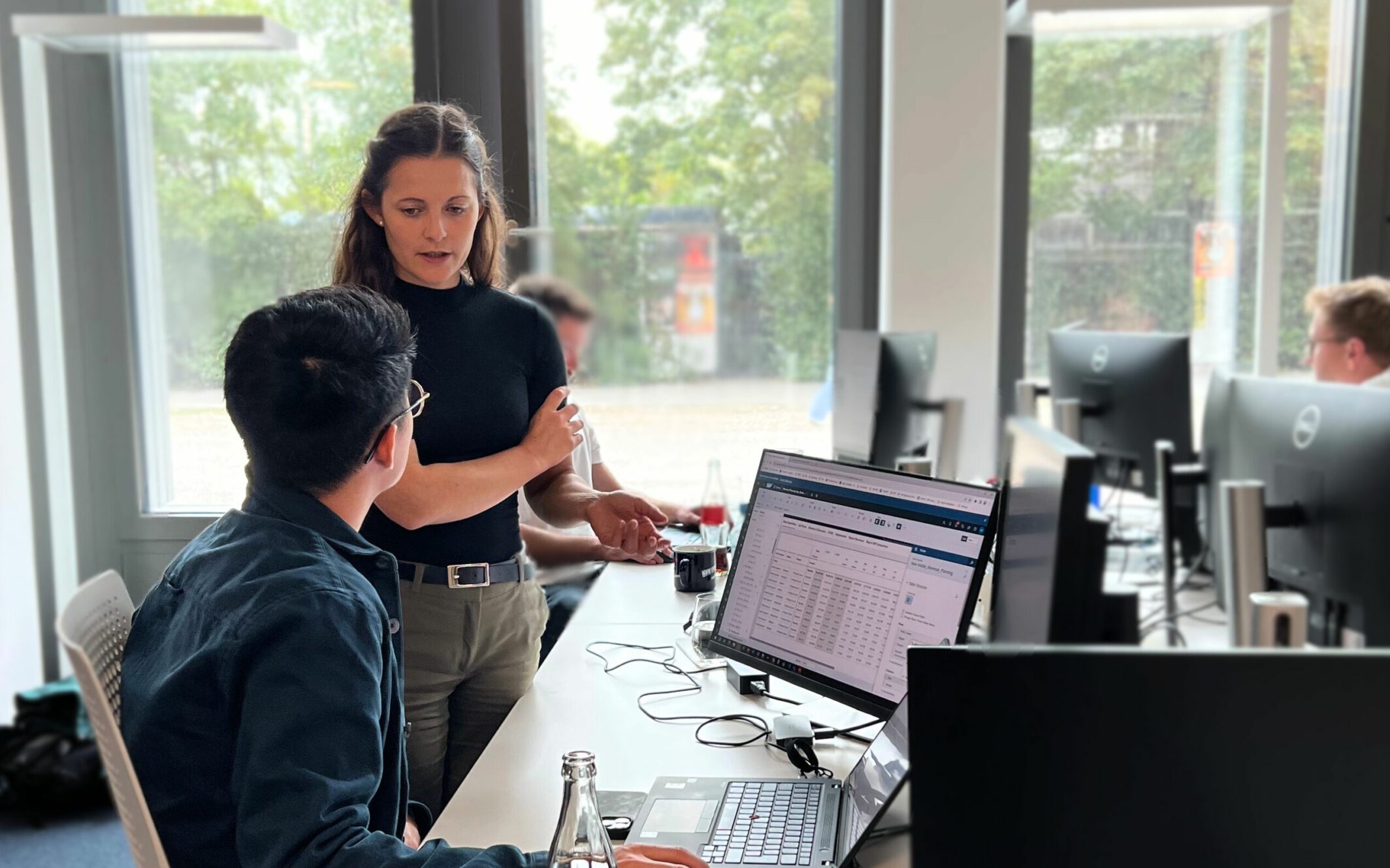 Eine Mitarbeiterin von valantic erklärt ihrem Kollegen am Schreibtisch, die Vor- und Nachteile von Hybrid- und Multi-Cloud-Strategien.