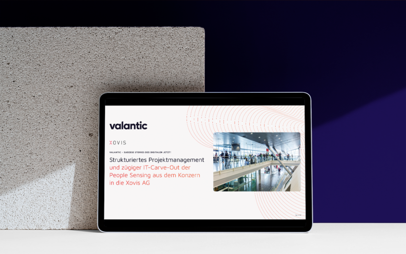 Auf einem strukturierten Block liegt ein Tablet mit der Präsentation „Strukturiertes Projektmanagement und IT-Carve-Out der People Sensing aus dem Konzern in die Xovis AG“ von valantic XOVIS.