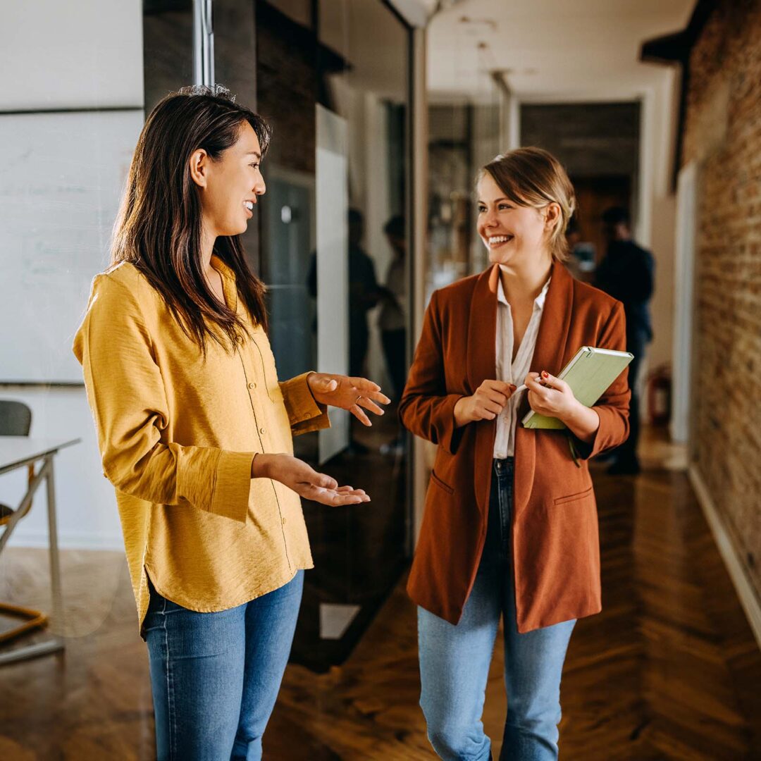 Two female colleagues talking in a hallway of modern office