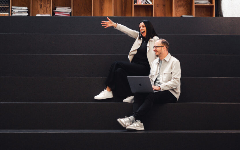 Three colleagues celebrate success in a modern office environment. Two people give each other a high-five while another person claps nearby.
