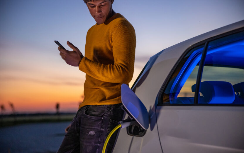 Man using mobile phone while charging electric car