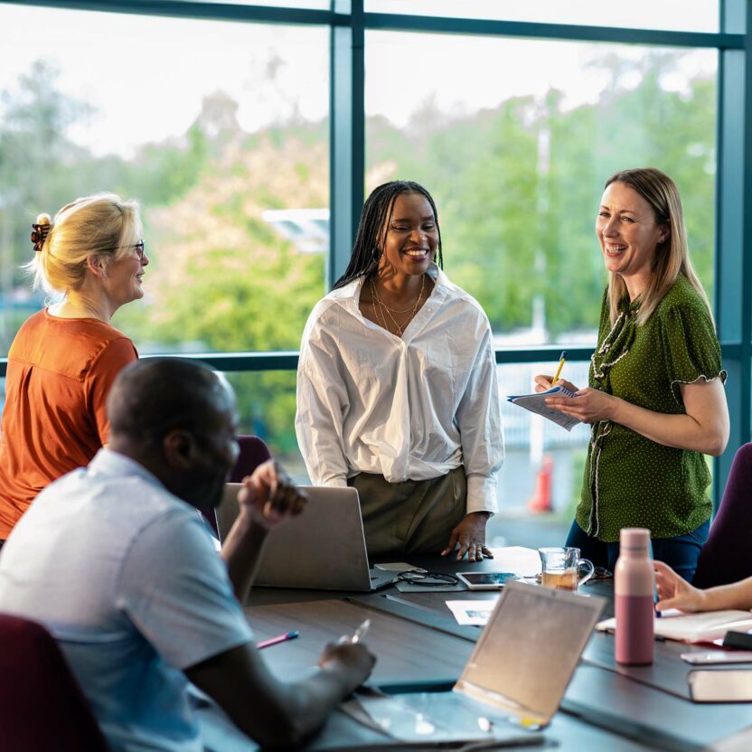An over-the-shoulder view of a group of cheerful co-workers having a team briefing and enjoying some time away from their desks and recounting funny stories from the office.