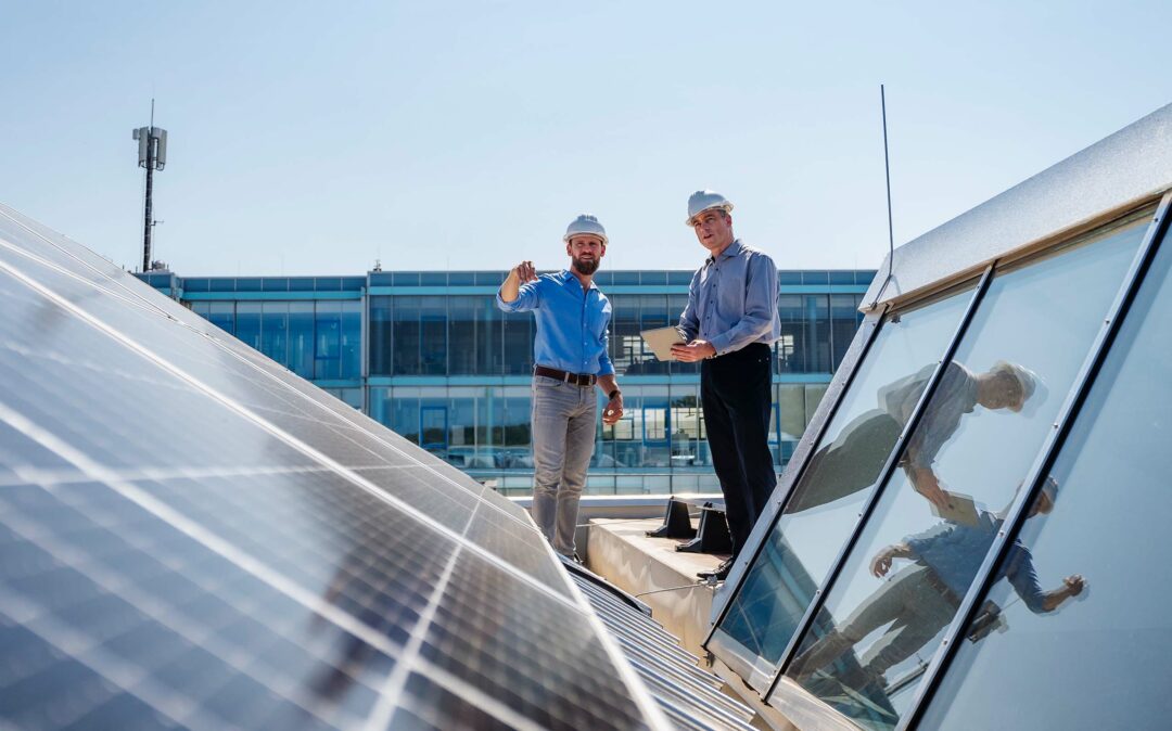 Two businessmen wearing hardhats having a meeting on the roof of a company building with solar panels