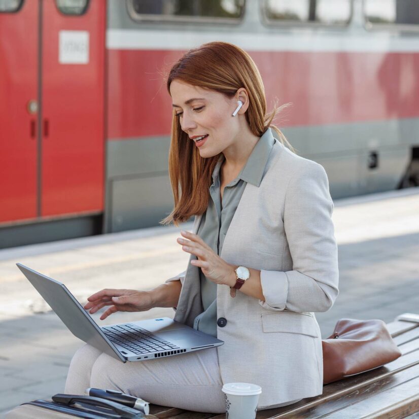 Businesswoman with in ear headphones using laptop at train station