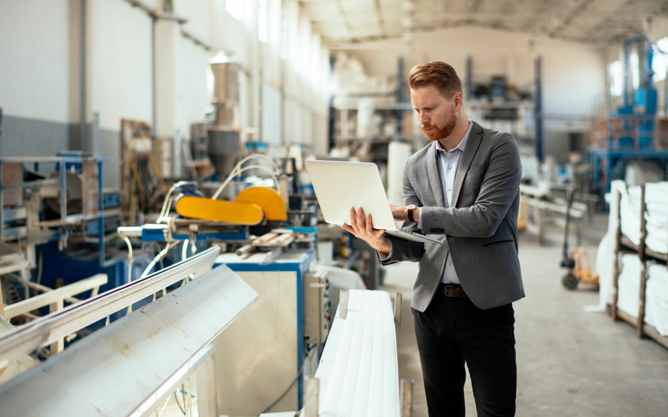 Angesteller steht in einer Fabrikhalle mit einem Laptop auf dem Arm