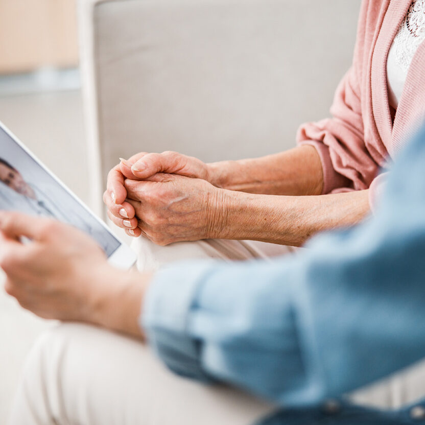Image of a woman with an elderly lady holding a tablet and making a video call to a doctor