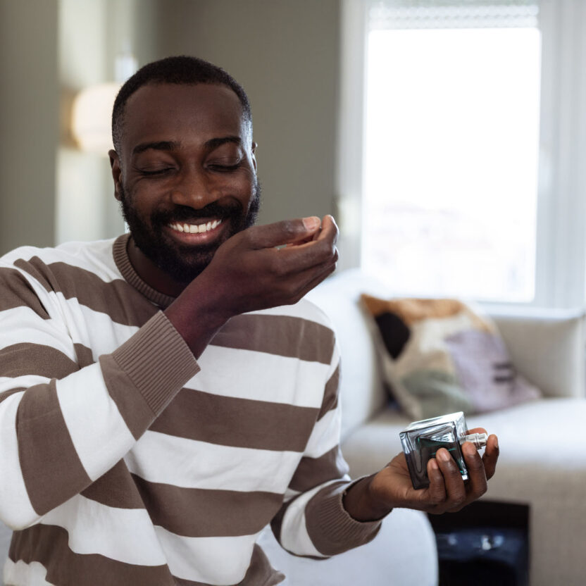 A cheerful man in a striped sweater smiles while enjoying the scent of a fragrance