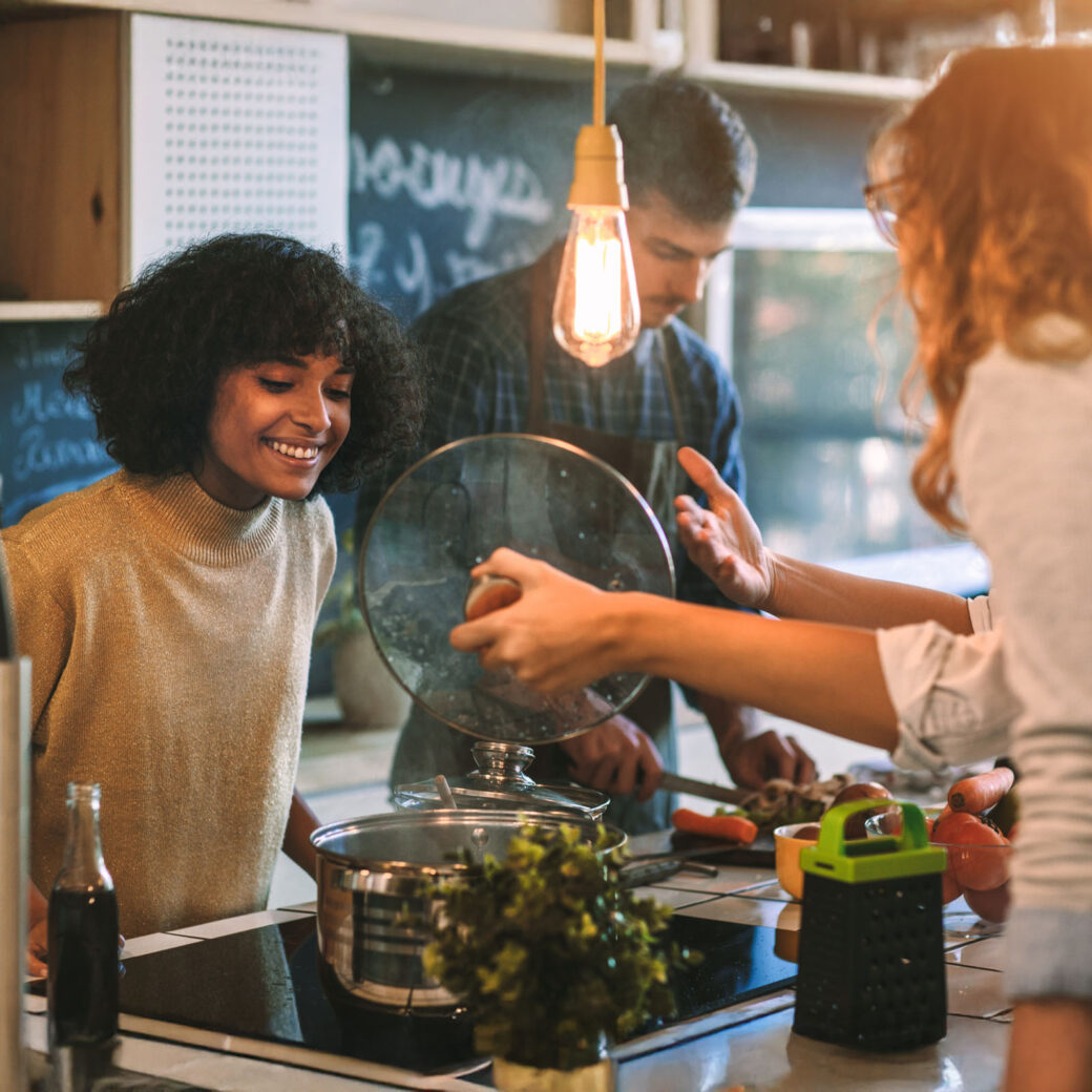 Friends Living And Cooking Together. Standing around the kitchen island, having fun and preparing food together
