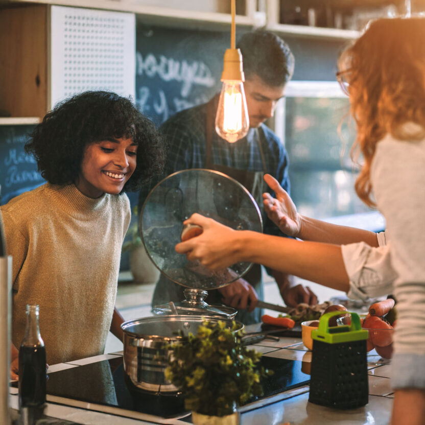 Friends Living And Cooking Together. Standing around the kitchen island, having fun and preparing food together