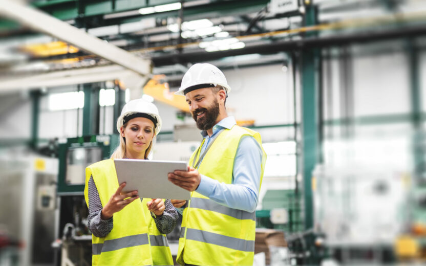 A portrait of a mature industrial man and woman engineer with tablet in a factory, talking.