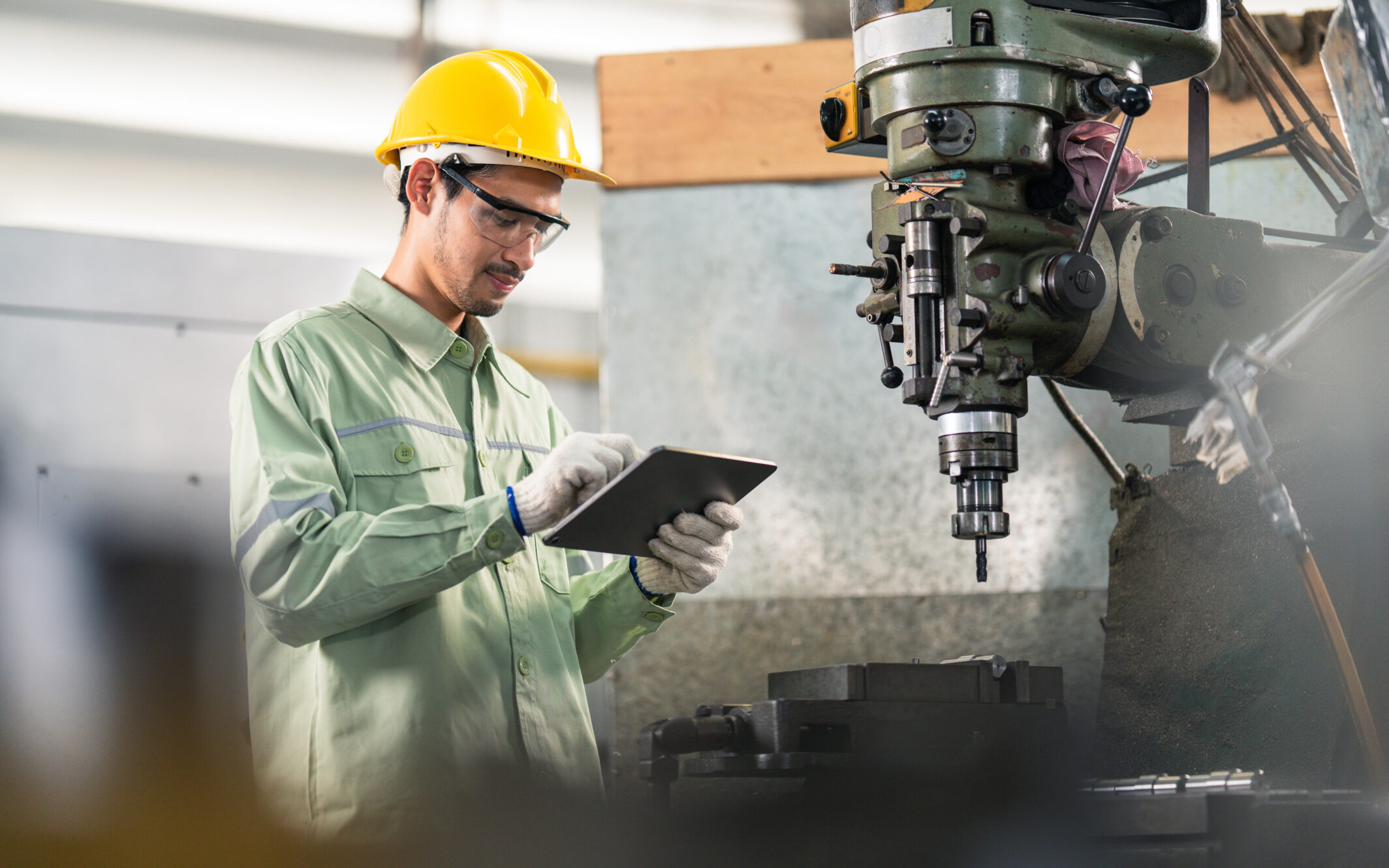 Techniker in einer Fabrikumgebung bedient ein Tablet neben einer großen Industriemaschine.
