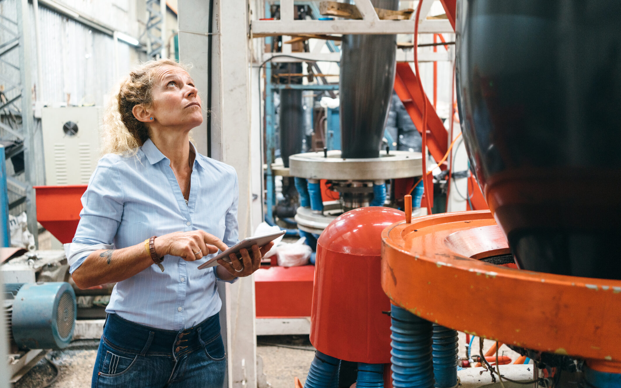 Person in Fabrik überwacht Maschinen mit einem Tablet.