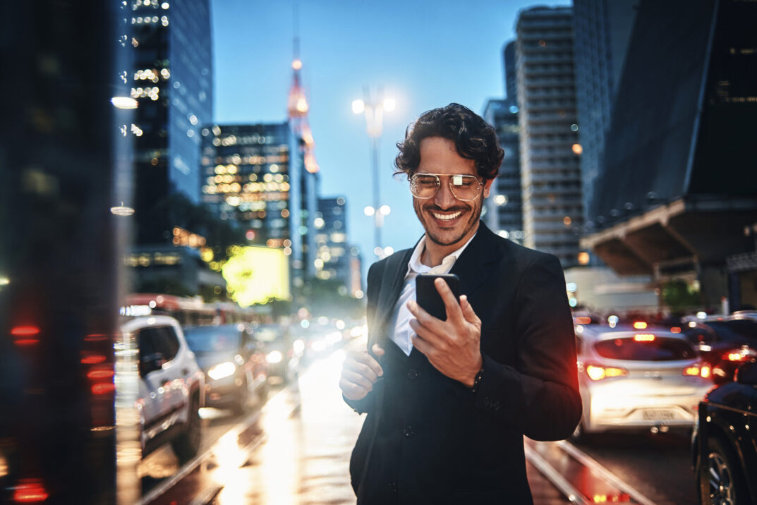 Lächelnder Geschäftsmann mit einem Handy in der Hand, Hintergrund Skyline einer Stadt | Agentic AI