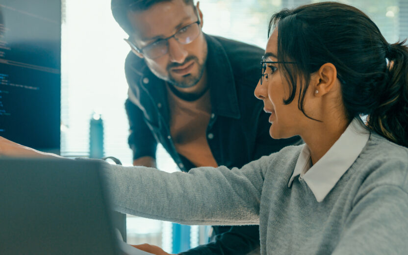 Two people discuss code on a computer screen, exploring how digitalisation is transforming insurance. One points at the screen to explain, while the other listens attentively.