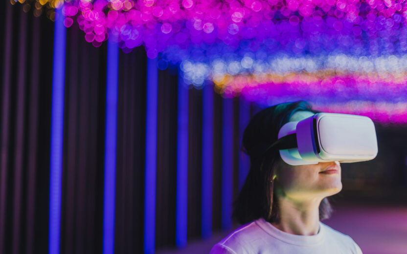 A person wearing a virtual reality headset stands under vibrant, colorful lights with pink, purple, and yellow hues in the background, reflecting the immersive impact of digitalisation in insurance.