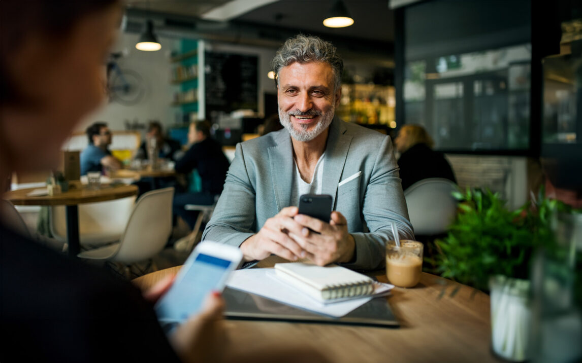 Man and unrecognizable woman having business meeting in a cafe, using smartphones.