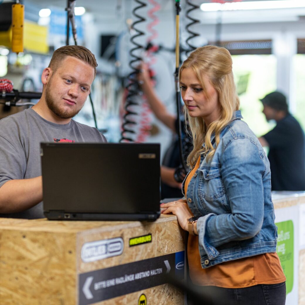 Two people are standing in the warehouse looking at a laptop