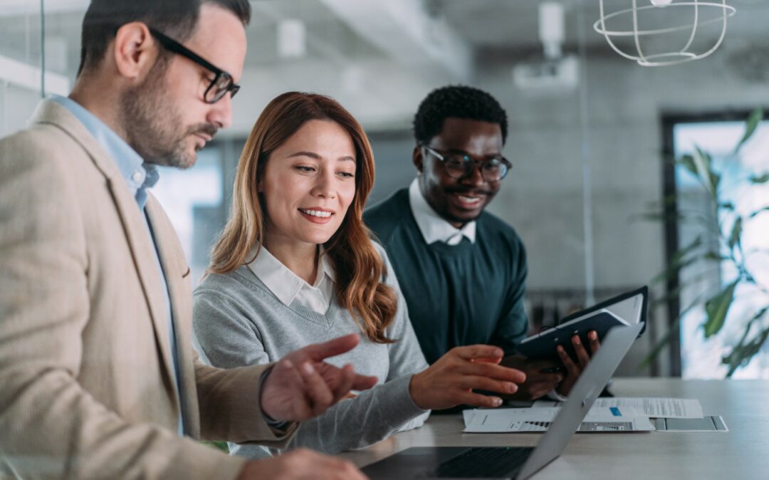 Drei Personen in Geschäftskleidung arbeiten gemeinsam an einem Schreibtisch und konzentrieren sich auf einen Laptop und ein Tablet. Dokumente und Büroausstattung bilden die Kulisse, während sie it-sicherheit Strategien für Incident Protection & Response gegen Ransomware-Bedrohungen diskutieren.