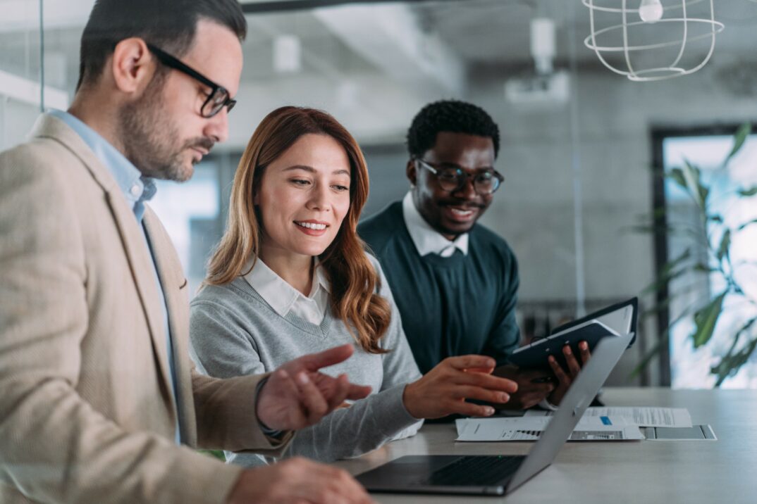 Drei Personen in Geschäftskleidung arbeiten gemeinsam an einem Schreibtisch und konzentrieren sich auf einen Laptop und ein Tablet. Dokumente und Büroausstattung bilden die Kulisse, während sie it-sicherheit Strategien für Incident Protection & Response gegen Ransomware-Bedrohungen diskutieren.