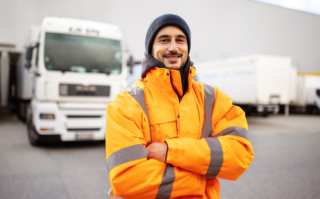 Portrait of a male commercial docker standing outdoors with arms crossed. Shipping yard worker with truck in background.