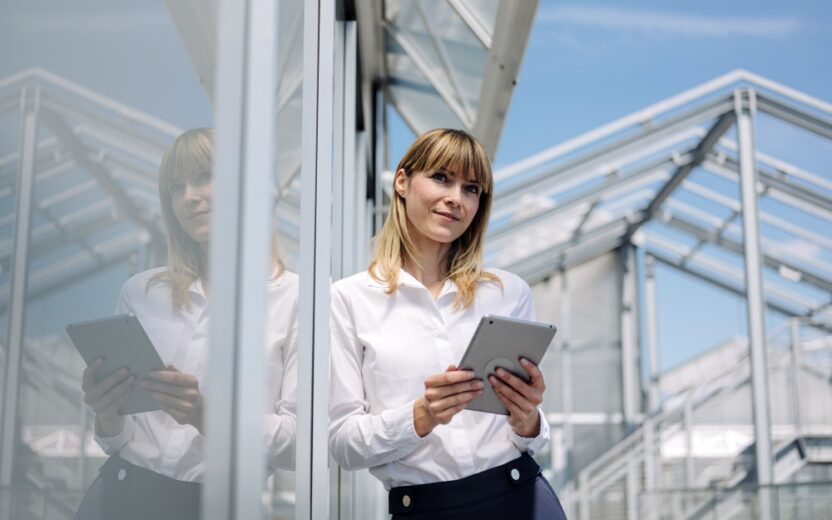 Thoughtful businesswoman holding digital tablet while standing by wall