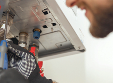 ine Person mit Bart arbeitet mit Werkzeugen an einem Gerät oder einer Maschine aus Metallkomponenten. Sie trägt schwarze Handschuhe mit weißen Punkten zum Schutz.