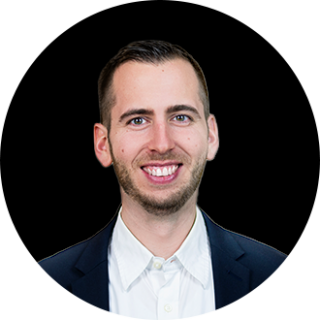 Ein Mann in dunkler Anzugsjacke und weißem Hemd lächelt vor einem schwarzen, runden Hintergrund in die Kamera und repräsentiert die valantic dmexco auf der dmexco2025.